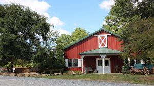 Rustic red barn at Cloer Family Vineyards surrounded by trees with outdoor benches and a vintage wagon.
