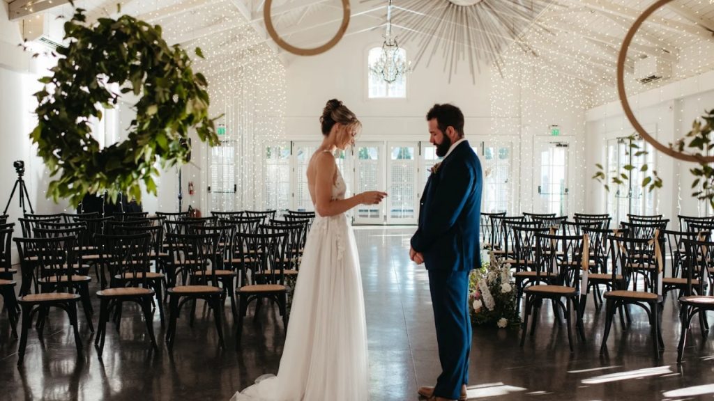 Bride and groom exchange vows inside the Merrimon Wynne with elegant string lights and classic décor.