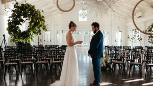 Bride and groom exchange vows inside the Merrimon Wynne with elegant string lights and classic décor.