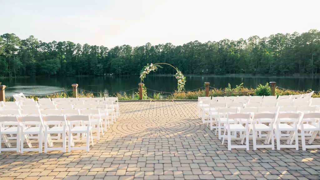 Outdoor wedding ceremony setup at the Pavilion at the Angus Barn with white chairs, floral arch, and lakeside view.