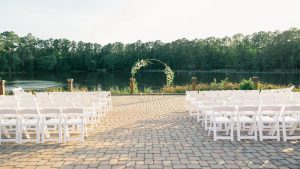 Outdoor wedding ceremony setup at the Pavilion at the Angus Barn with white chairs, floral arch, and lakeside view.