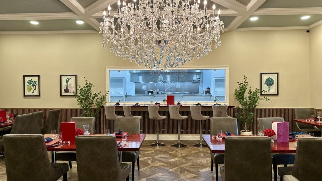 Elegant dining area at Rayson Winery & Vineyards with Bistro Europa Restaurant featuring a crystal chandelier, modern seating, and an open kitchen view.