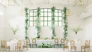 Elegant wedding reception setup at The Distillery with white walls, greenery accents, and modern chandeliers.