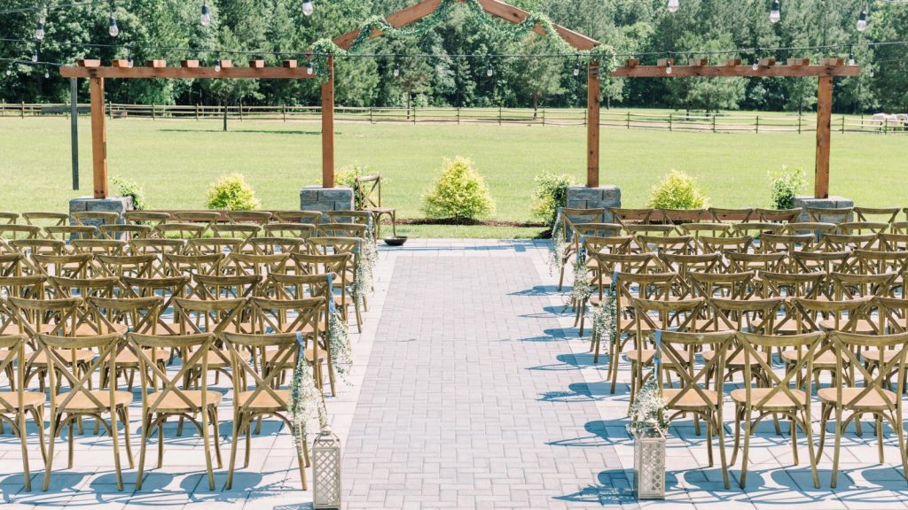 Outdoor wedding ceremony setup at The Evermore with wooden chairs, string lights, and a rustic arbor overlooking open fields.