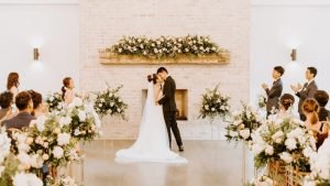 Bride and groom share a kiss during their wedding ceremony at The Maxwell with floral arrangements and elegant décor.