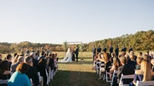 Outdoor wedding ceremony at The Meadows with bride, groom, bridal party, and guests in a scenic field setting.