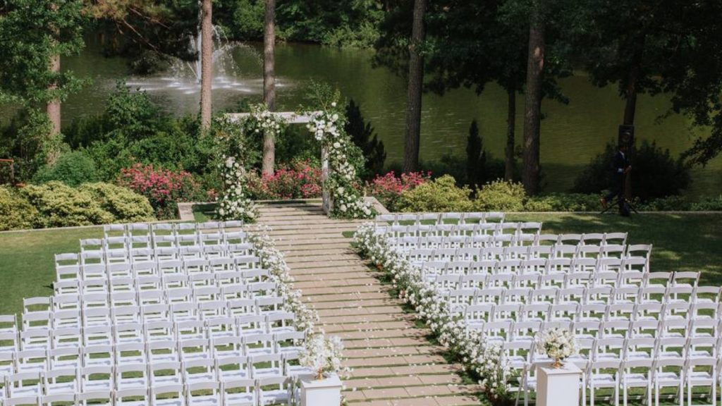 Outdoor ceremony setup at The Umstead Hotel and Spa Wedding Venue with white chairs, floral arch, and lake backdrop.